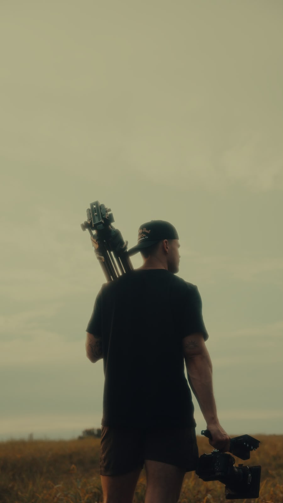Bennett Looper carrying a tripod and camera through a field at dusk